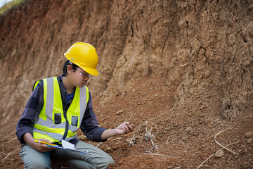 young male construction worker observing and examining the soil structure in the field and then recording it