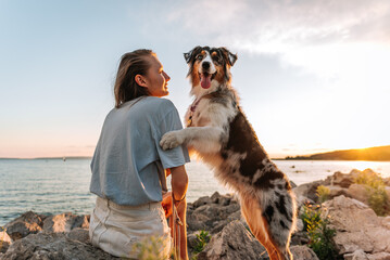 a girl and an Australian Shepherd dog are sitting on the rocks on the river bank; friendship between man and dog