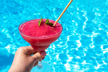 Hand with chilled raspberry Daiquiri with mint in hand by pool on sunny day. Concept of summer fun...