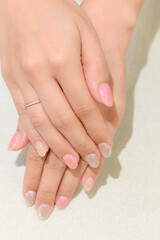 Elegant hands with manicured nails featuring gradient design, showcasing blend of soft pink and glittery tips.