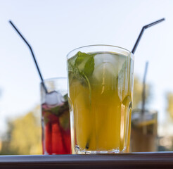 A glass of orange juice sits on a table next to two other glasses