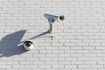 Surveillance security camera mounted on a white brick wall in active monitoring position. High quality picture for download