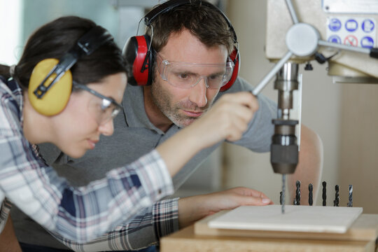 apprentice standing at drill press and listening to her mentor