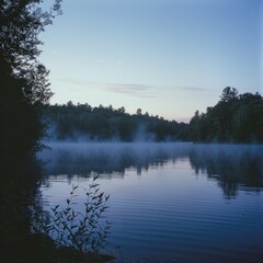 A panoramic view of a serene lake at dawn, with mist rising from the surface and the first rays of sunlight piercing through the dense forest in the background
