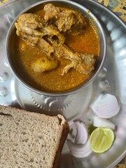 Maharashtrian Chicken Gravy with Chicken Drumstick and Brown Bread and Onion slices on a steel plate