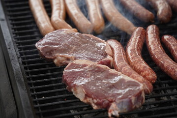 Sausages and pieces of meat are fried on the surface of the grill.