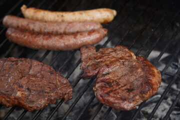 Sausages and pieces of meat are fried on the surface of the grill.