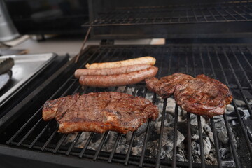 Sausages and pieces of meat are fried on the surface of the grill.