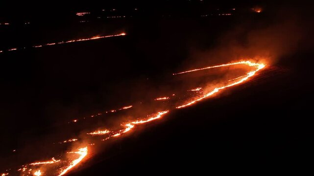 Raging fire at the dry grass meadow. Agricultural field fire burning. Night aerial footage of smoke and flame. Firefighters emergency response. Ecological catastrophe and environmental hazard.