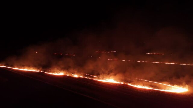 Raging fire at the dry grass meadow. Agricultural field fire burning. Night aerial footage of smoke and flame. Firefighters emergency response. Ecological catastrophe and environmental hazard.