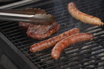 Sausages and pieces of meat are fried on the surface of the grill.