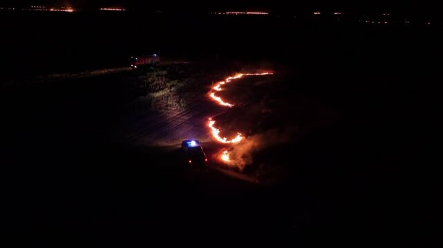 Raging fire at the dry grass meadow. Agricultural field fire burning. Night aerial footage of smoke and flame. Firefighters emergency response. Ecological catastrophe and environmental hazard.