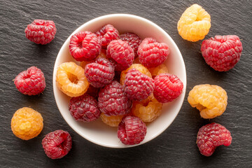 Fresh sweet raspberry with ceramic plate on slate stone, macro, top view.