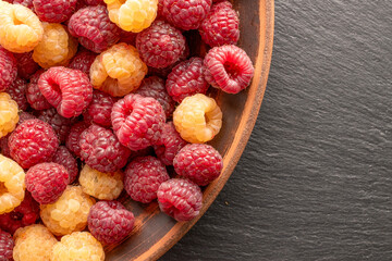 Fresh sweet raspberry with clay plate on slate stone, macro, top view.