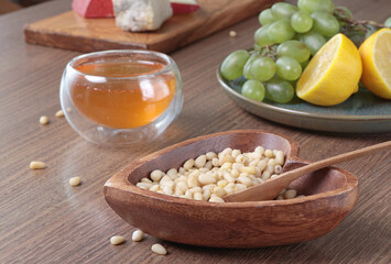 Fresh honey pour into glass bowl. Pine nuts in heart shaped plate. Wooden dishes and food on table. Useful natural food. 