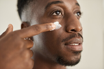 Young African man applying moisturizer to his cheek using a finger