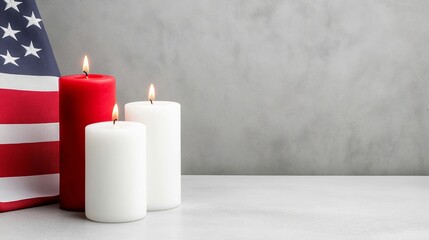 Three candles are lit on a table in front of an American flag. The candles are red and white, and they are lit up. The candles are arranged in a row, and they are placed on a gray surface