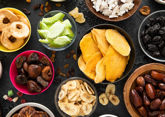 Assorted organic healthy dried sweet berries and fruits snack in various bowl plates on black background.Top view.