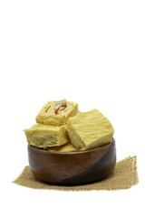 Soan Papdi or Shompapri Garnished with Cashew Nut, Pistachio, Almond and Saffron in Wooden Bowl with Burlap Fabric Isolate on White Background with Copy Space, Also Known as Patisa or Shonpapdi