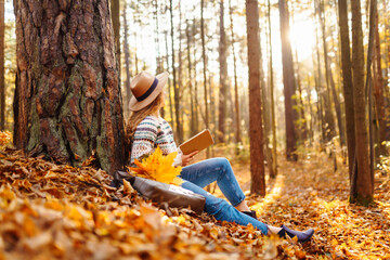 A woman enjoys reading in a peaceful forest during autumn while sitting beside her bicycle on...