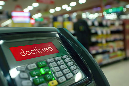 Credit card terminal with a declined message in a store, representing a failed transaction, with a blurred background of retail items.