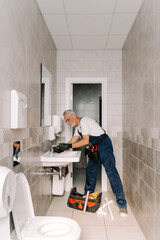 Senior plumber repairing a faucet in a public bathroom