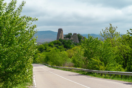 View from the road to the Ujarma fortress standing on a cliff. Green trees around. Mountains in the background