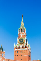 The iconic Spasskaya Tower of the Moscow Kremlin, featuring a large clock and topped with a red star, set against a clear blue sky.