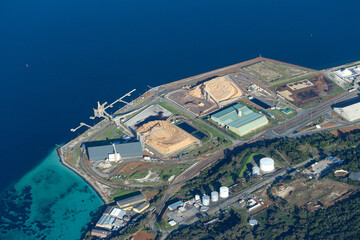Obraz premium Albany WA shipping port and dock, with large warehouses and machinery along with cranes and piles of sand. Deep blue still water on the left side of the dock. Green grassy hillside. Stick photo.