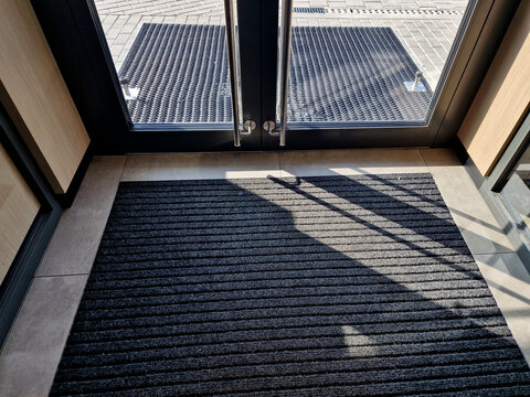 industrial mat cleaning zones at the entrance to the building. A black plastic-metal mat in the shape of an arch or half-circle lies on the limestone mosaic tiles
