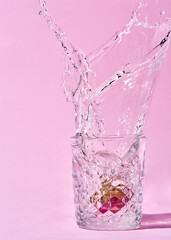 A splash of water bursts from a glass filled with ice cubes and a slice of citrus fruit. The water droplets are frozen in mid-air