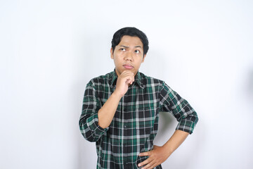 thoughtful indonesian young man looks confused standing over isolated white background wearing...