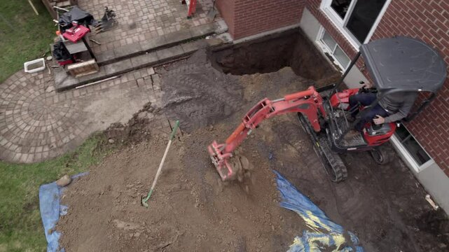 Small excavator digs up house foundation for repairs - aerial shot