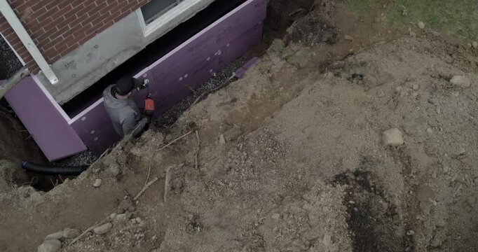 Construction worker instaling insulation on foundation of residential house in autumn