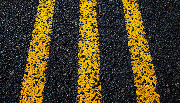 Three parallel yellow lines painted on a rough, textured asphalt surface.