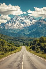 Fototapeta premium Scenic Road Leading to Majestic Snow-Capped Mountains Under a Clear Blue Sky with Fluffy Clouds