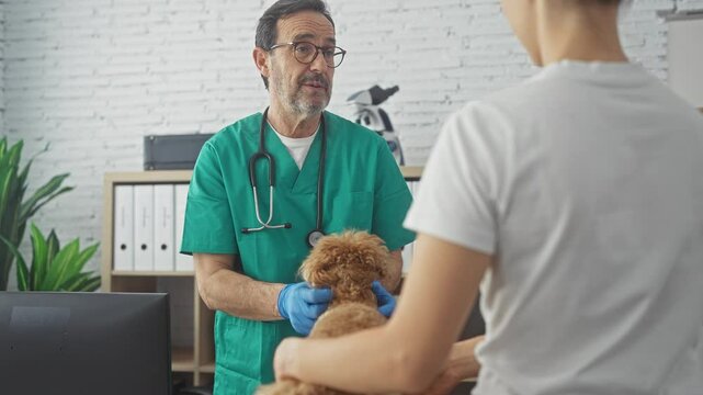 A concerned male veterinarian examines a poodle held by its owner in the clinic's examination room.