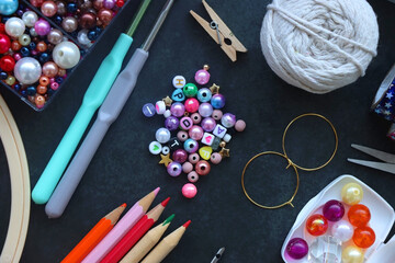 Colorful beads, coloring pencils, glitter, needles, string, hoop, tape and scissors on dark...
