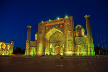 Sherdor Madrasah on Registan Square illuminated at night.
