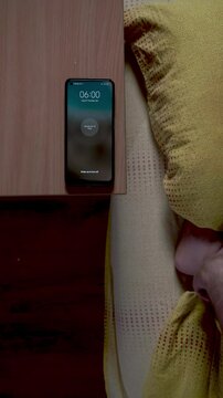 Alarm clock on phone. The clock on the phone shows six in the morning, on the bedside table in the bedroom. Man turns off smartphone alarm clock in the morning