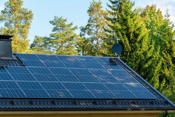 solar panels on home roof against blue sky and trees. green energy concept.