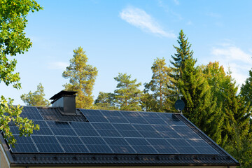 solar panels on home roof against blue sky and trees. green energy concept.