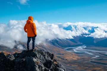 Obraz premium Hiker in Orange Jacket Admiring Mountain View, Snow-Capped Peaks and River Valley