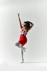 A confident young woman with curly hair showcases her vibrant red outfit while striking a playful pose.