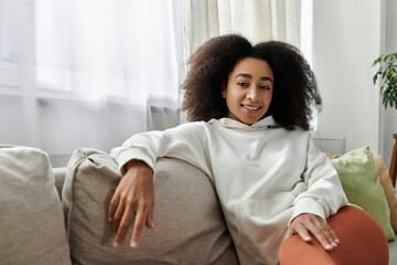 A young woman relaxes in her cozy attire, smiling comfortably in her living room.