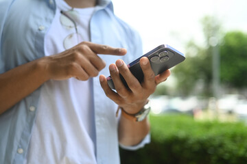 Cropped shot of man typing text message on mobile phone, standing outdoor