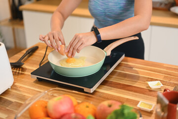 Cropped shot of young woman wearing active ware frying eggs for breakfast in kitchen