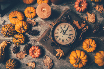 Festive autumn still life with vintage alarm, pumpkins and candles on wooden surface on brown background