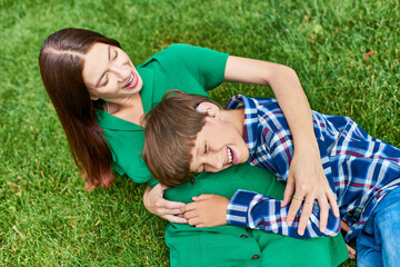 A mother and her hearing impaired son enjoy playful laughter in a vibrant green field.