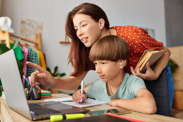 A mother engages with her son, guiding him as he learns at their cozy workspace.